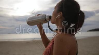 迷人的年轻混血女模特饮水瓶在海滩日落。 高清慢速运动。 泰国Koh Phangan